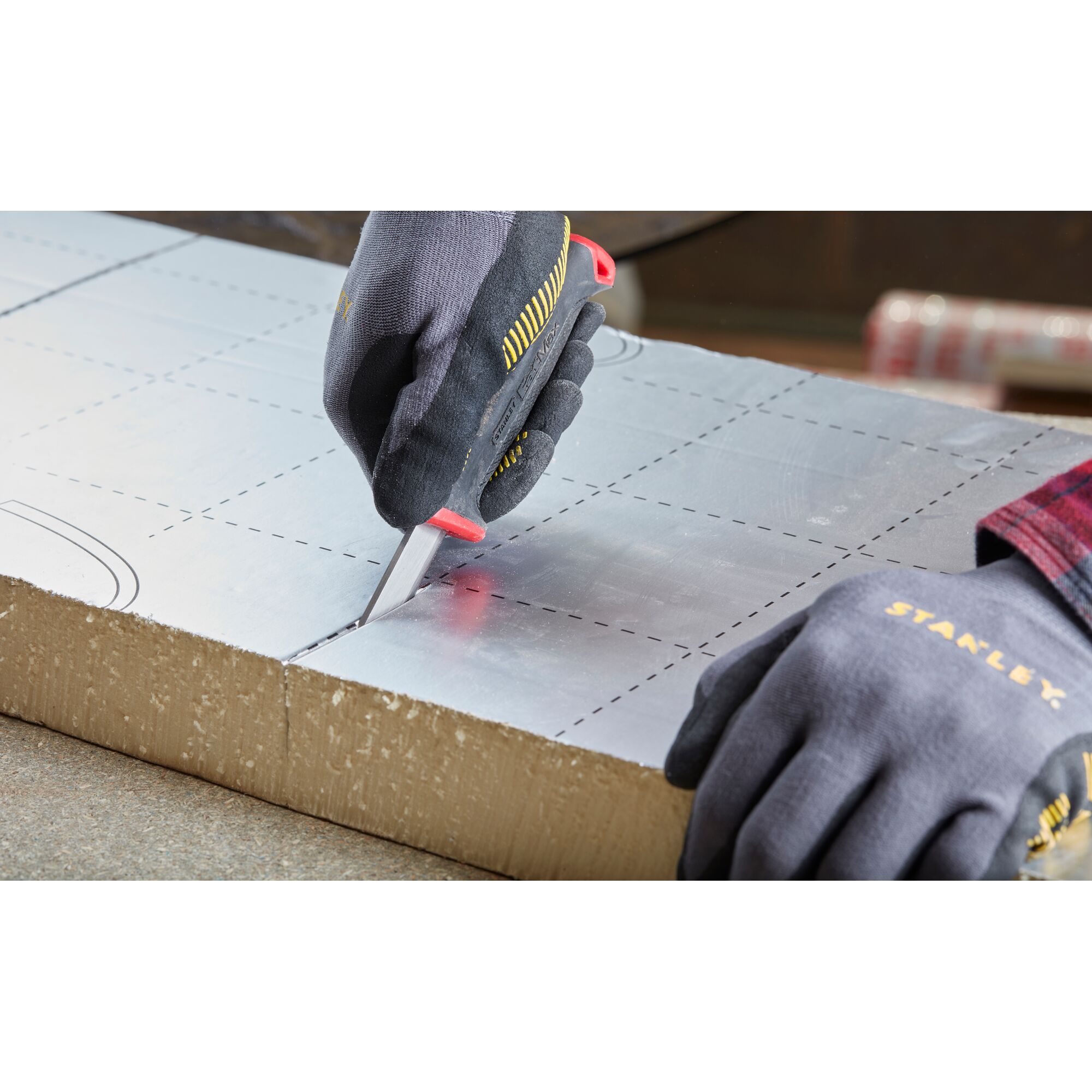 Photo of STANLEY 0-10-231 utility knife cutting foil-faced insulation board, close-up angle, hands wearing gloves.