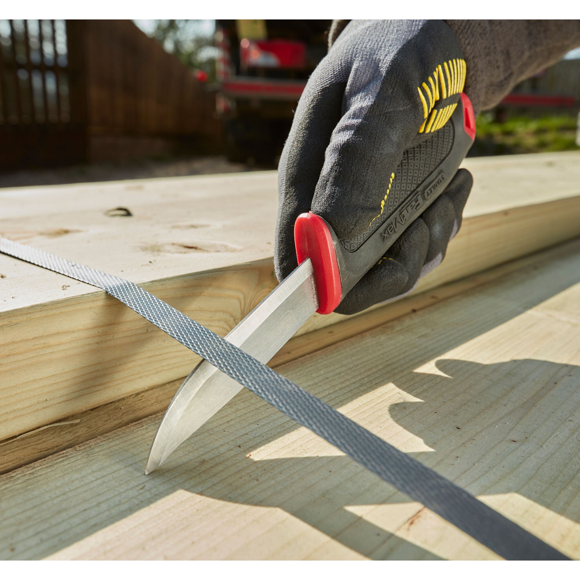 STANLEY 0-10-231 photography of utility knife with black and red handle held on wooden planks outdoors.