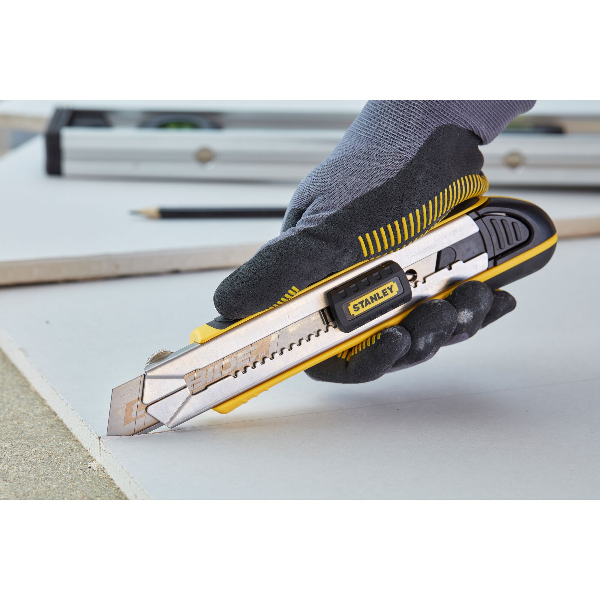 STANLEY 0-10-481 utility knife cutting drywall, ergonomic handle, silver and yellow finish, close-up side view.