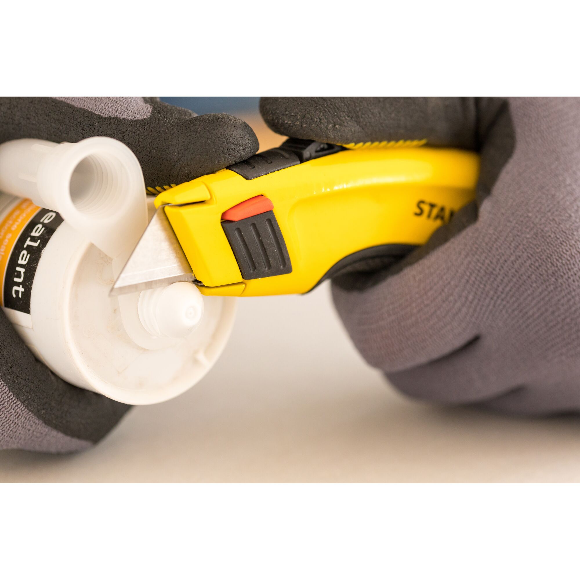 Photo of STANLEY 0-10-778 utility knife cutting plastic tube, close-up view, hands in gloves holding both items.