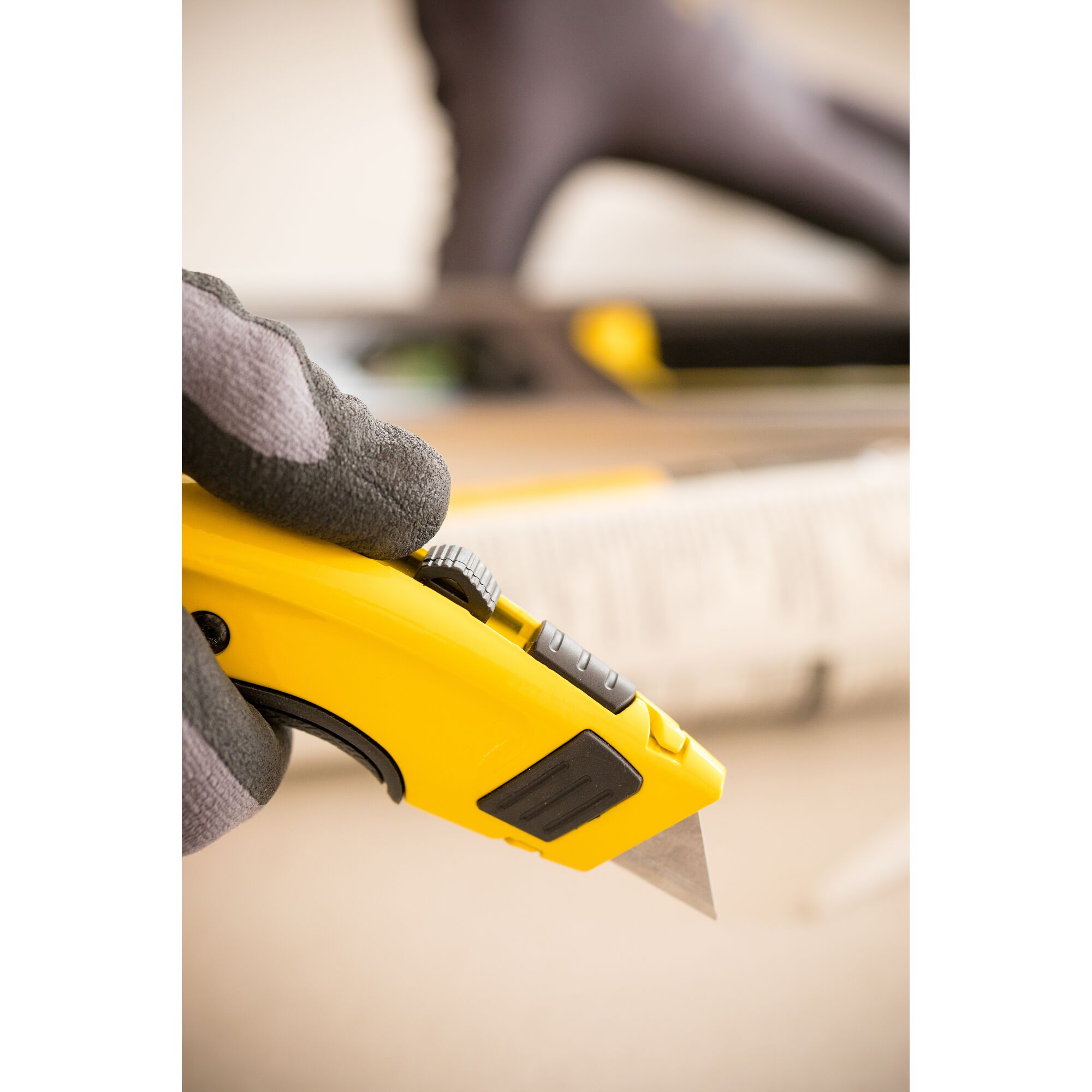 Photo of STANLEY 0-10-778 utility knife held in gloved hand, close-up view showing yellow body and exposed blade.