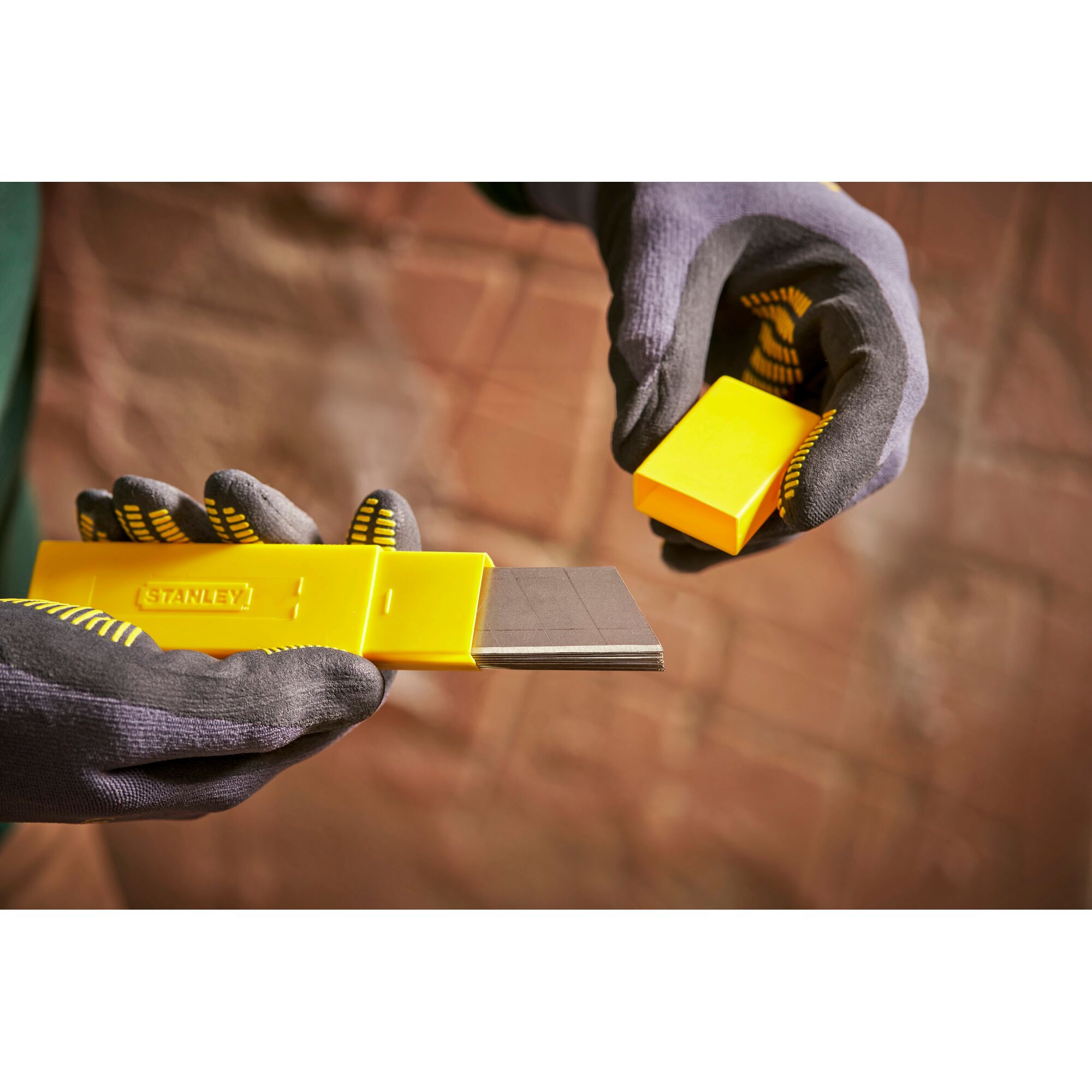 STANLEY 0-11-325 yellow blade dispenser held in gloved hands, showing multiple utility blades.