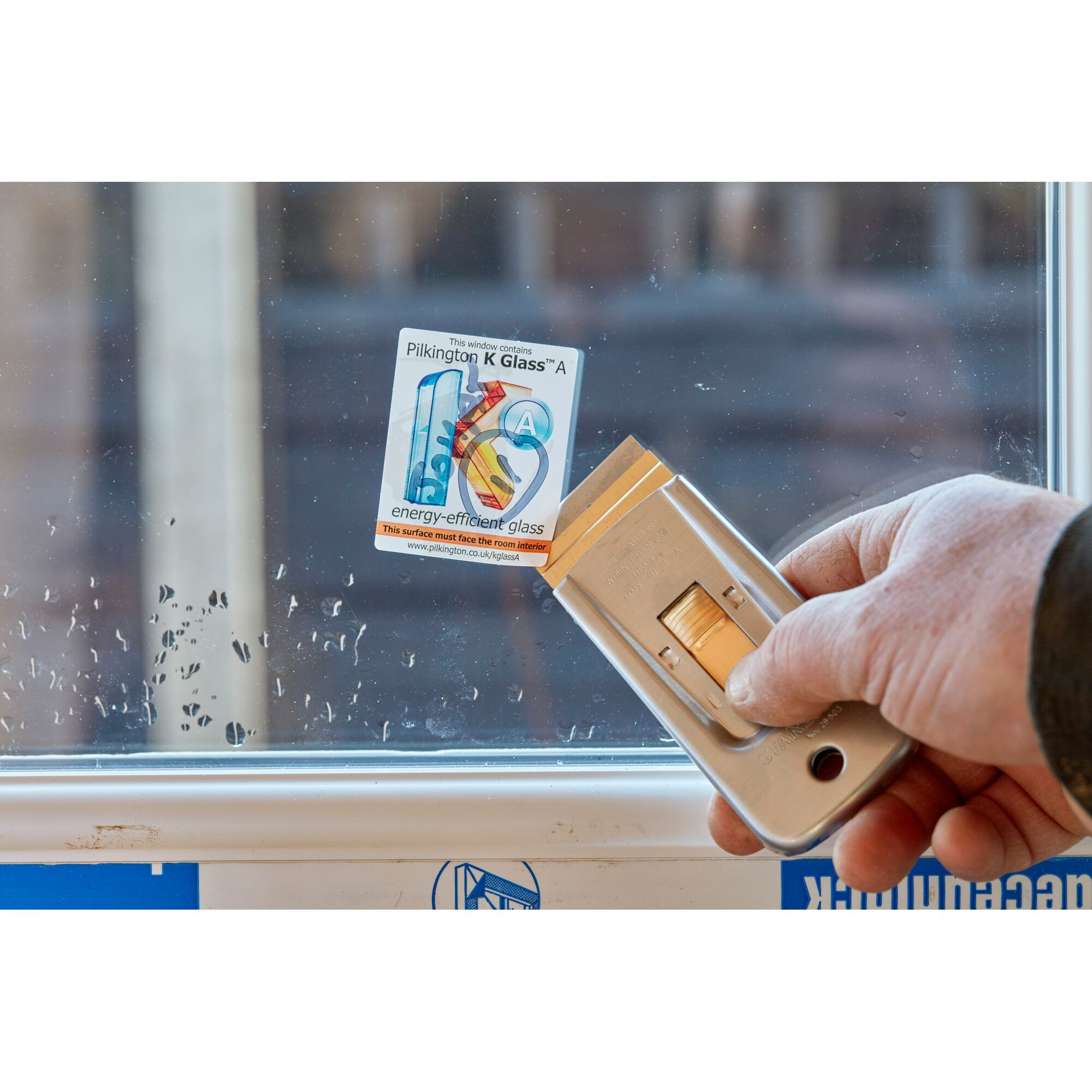 STANLEY 0-28-500 window scraper removing a sticker from glass, close-up of tool in use.