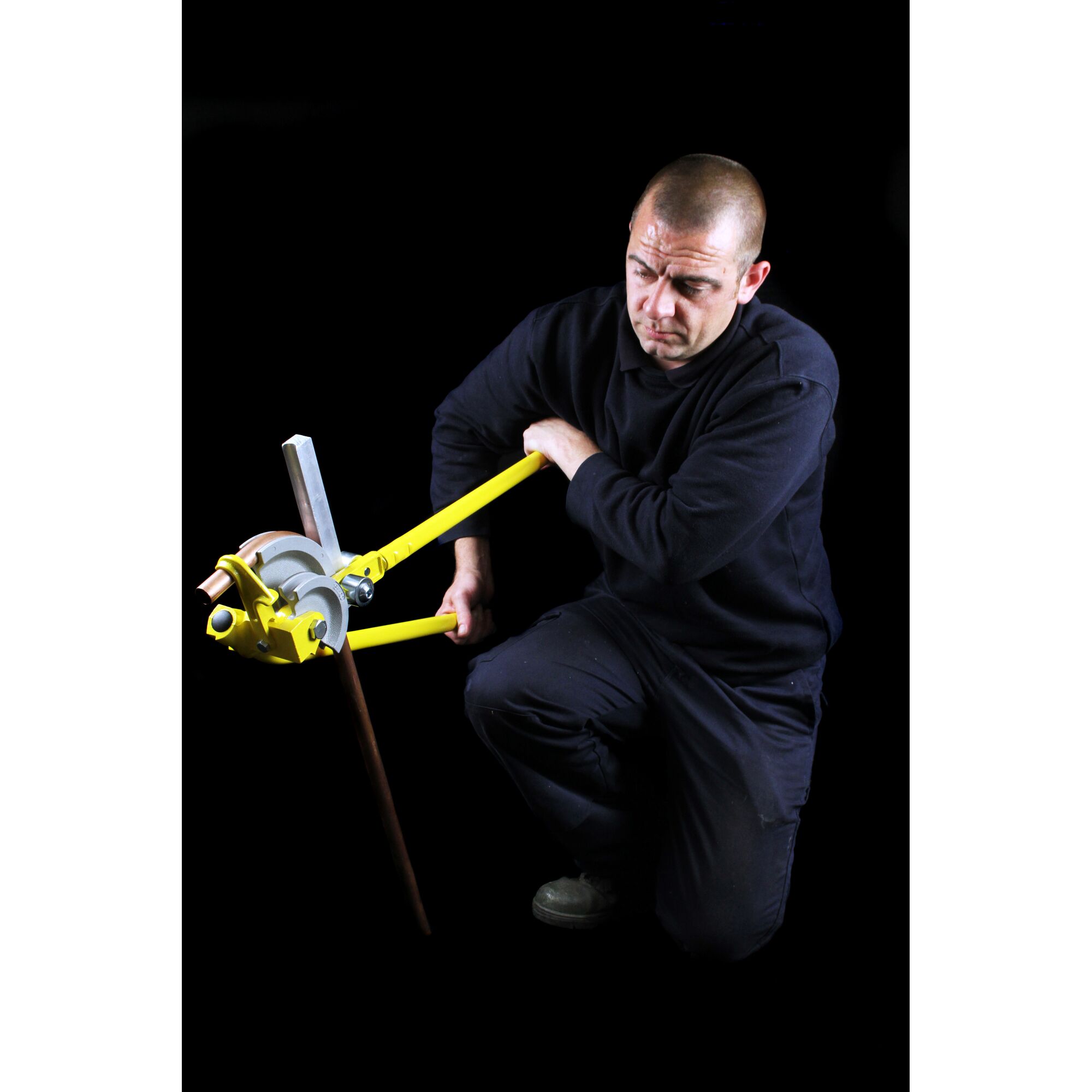 Photo of a person using STANLEY 0-70-452 pipe bender tool on a metal pipe, against a black background.