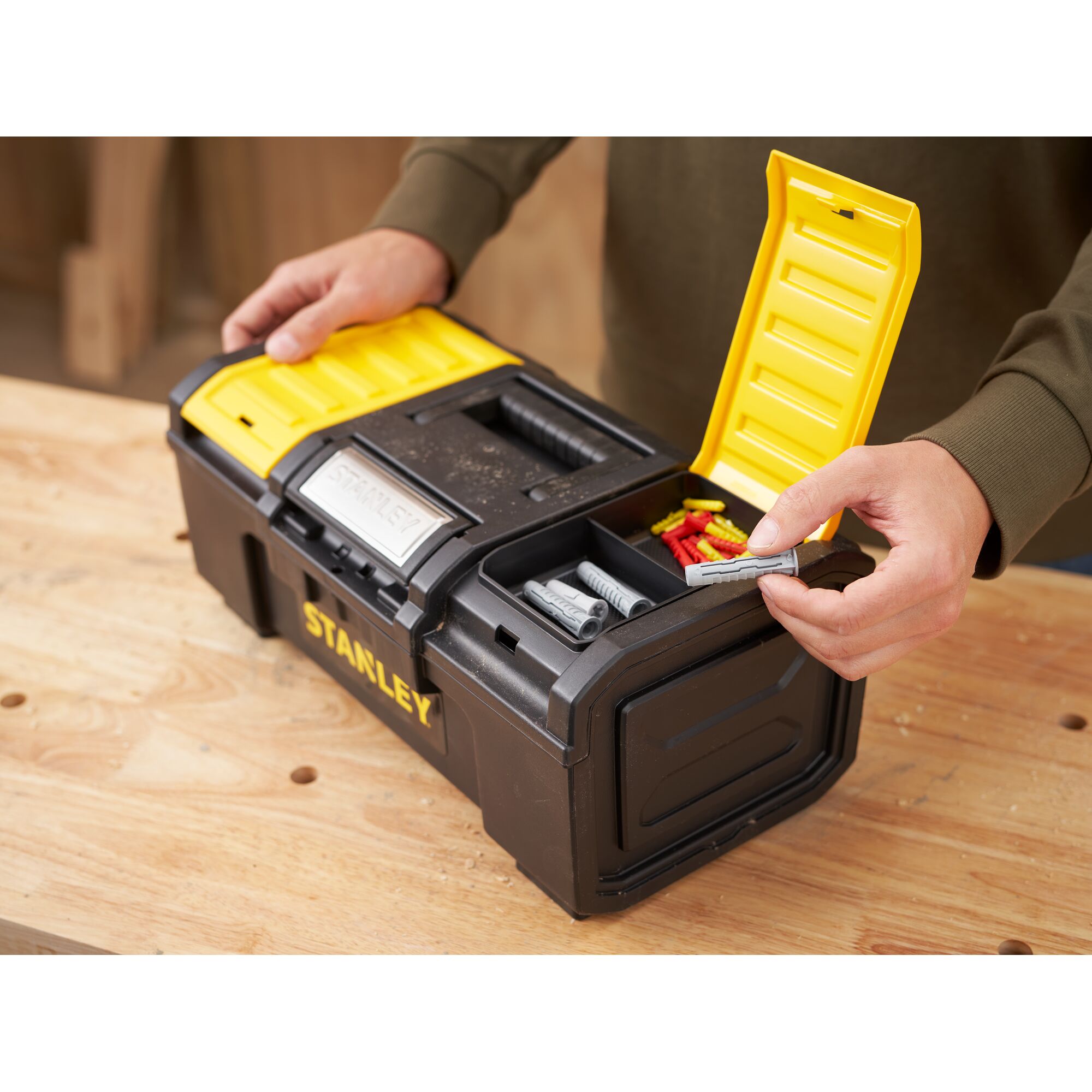 STANLEY 1-79-216 black and yellow toolbox with open compartment holding wall plugs, shown on a workbench.