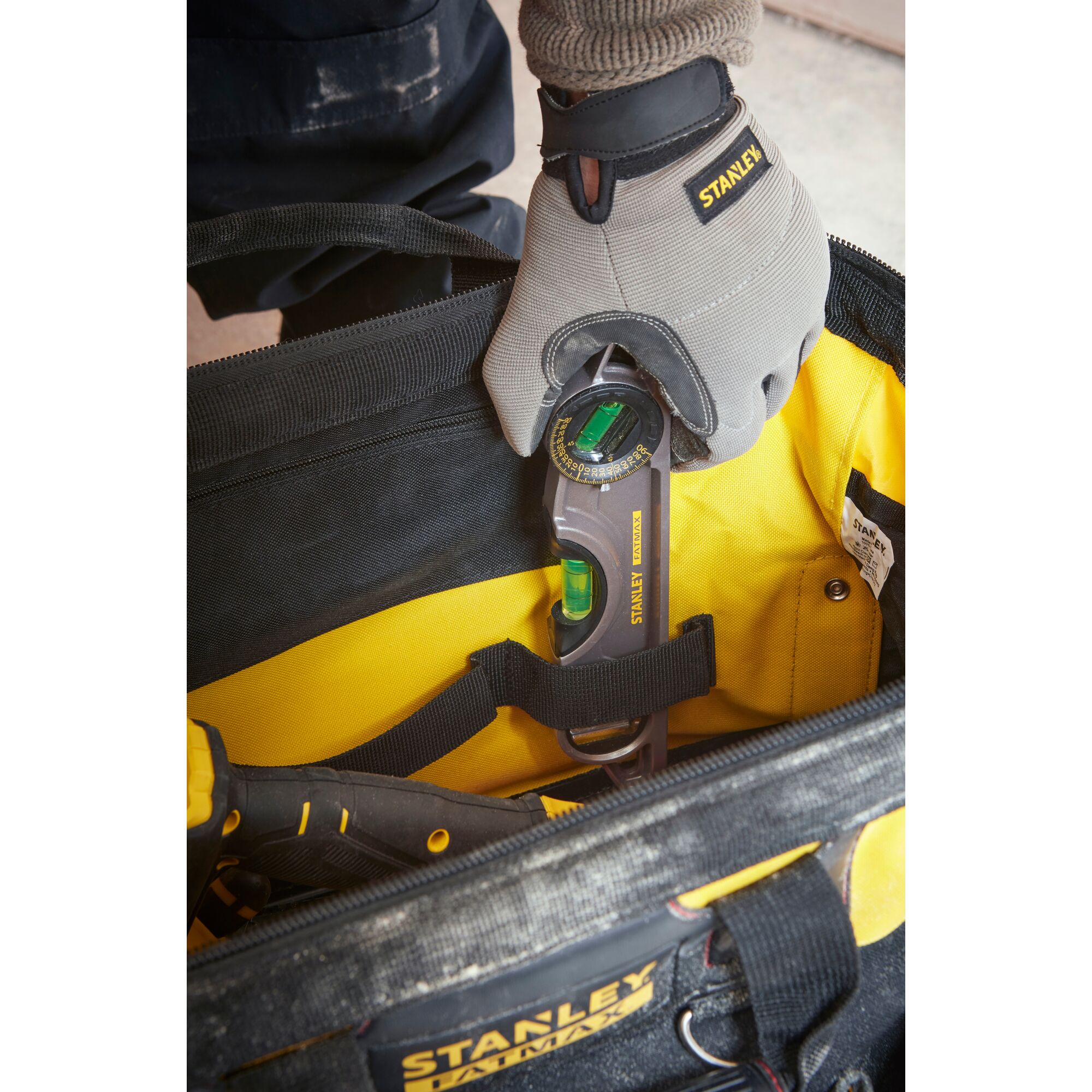 Photo of STANLEY 1-93-950 tool bag with worker placing digital angle gauge inside, close-up top view.