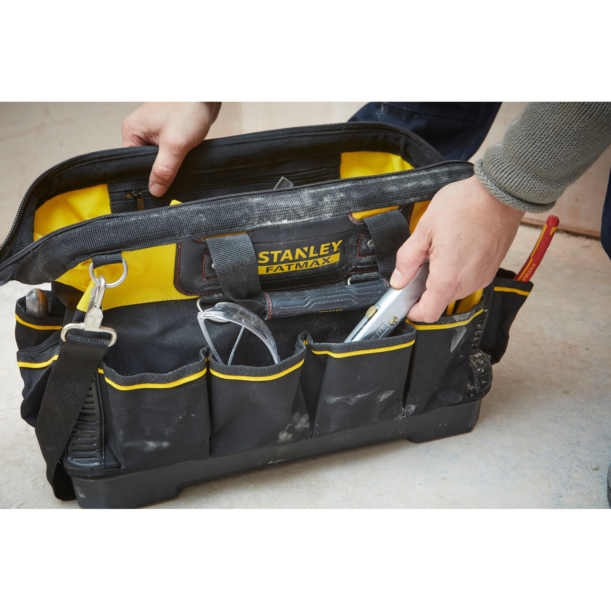 STANLEY 1-93-950 tool bag with yellow and black design, open with hand, tools and safety glasses visible.