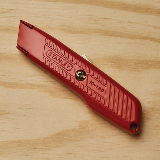 Self retracting safety utility knife placed on wooden surface.