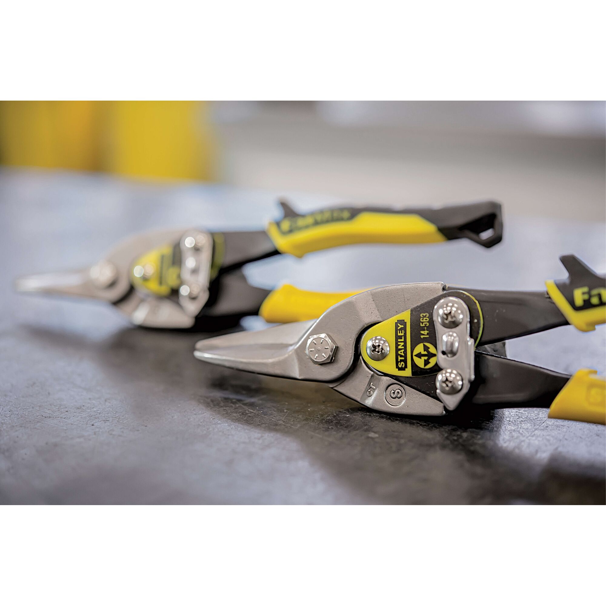 Photo of STANLEY 14-563 aviation snips with yellow handles on a work surface, angled side view.