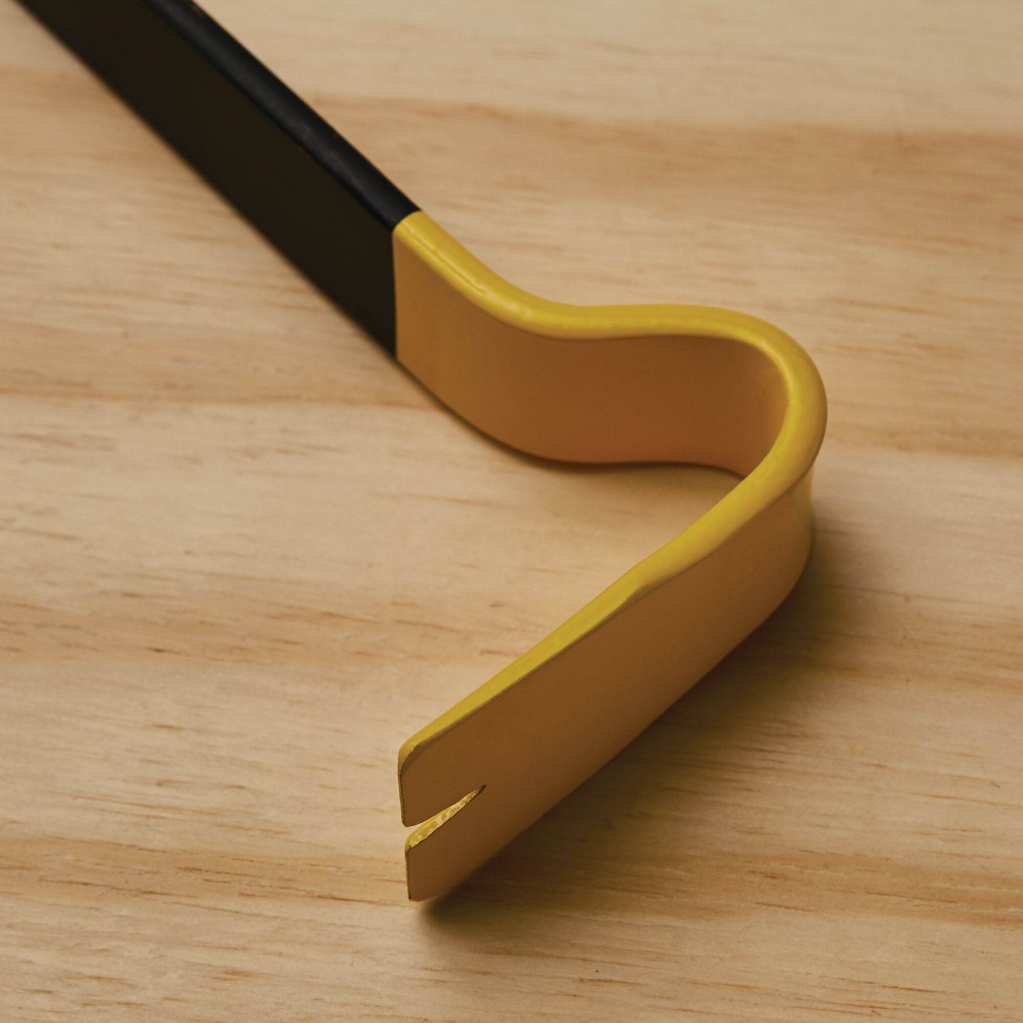 STANLEY 55-526 yellow and black pry bar close-up on wood surface, curved end with nail slot.
