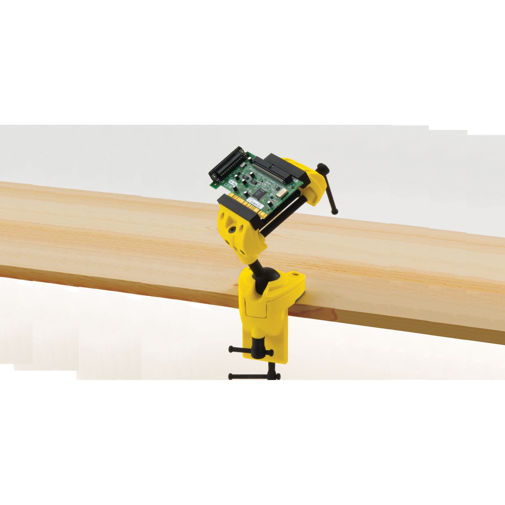 STANLEY 83-069 yellow bench vise clamped to wood plank, holding a small circuit board, product side angle.