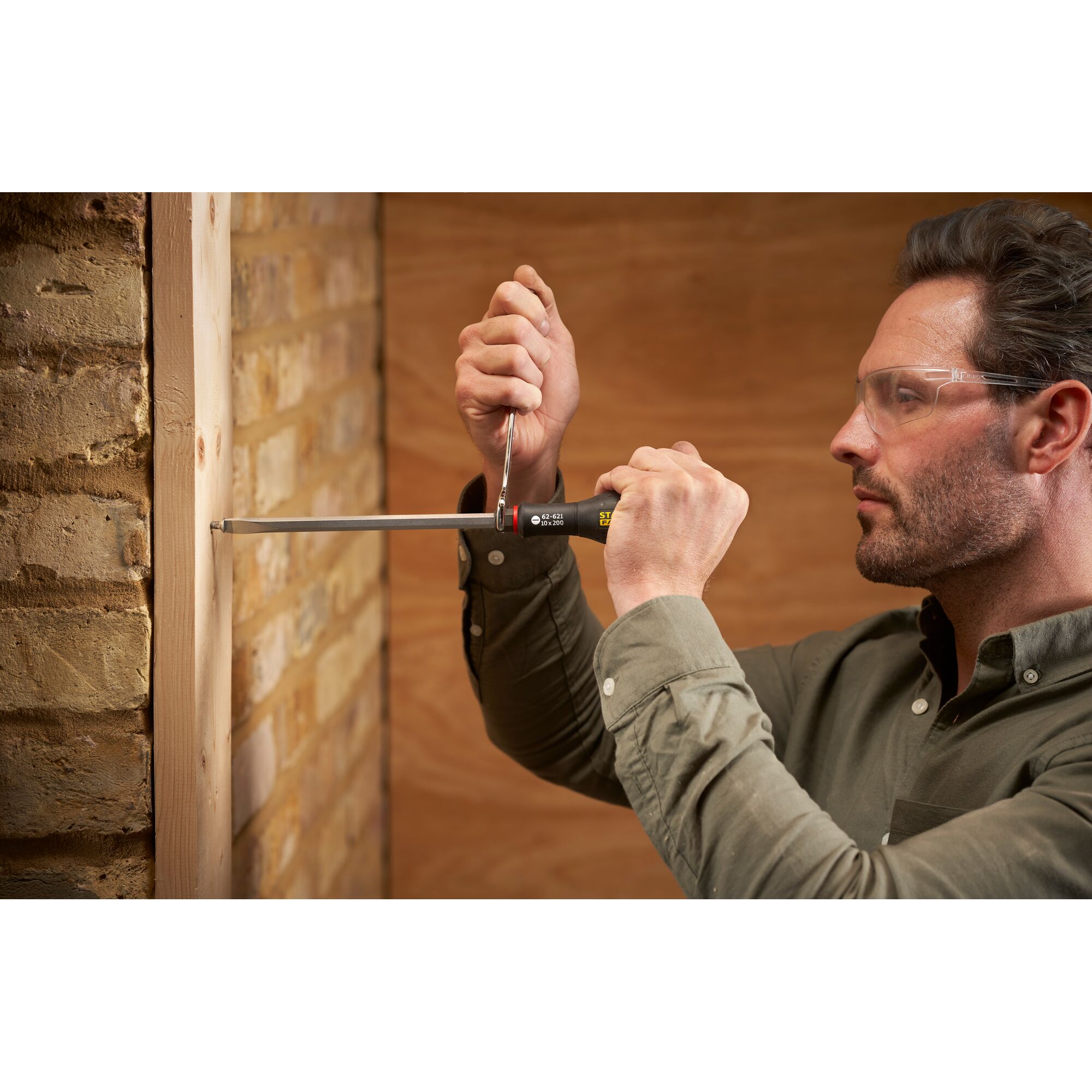 Photo of STANLEY FMHT0-62621 screwdriver used to fasten screw in wooden frame against brick wall.