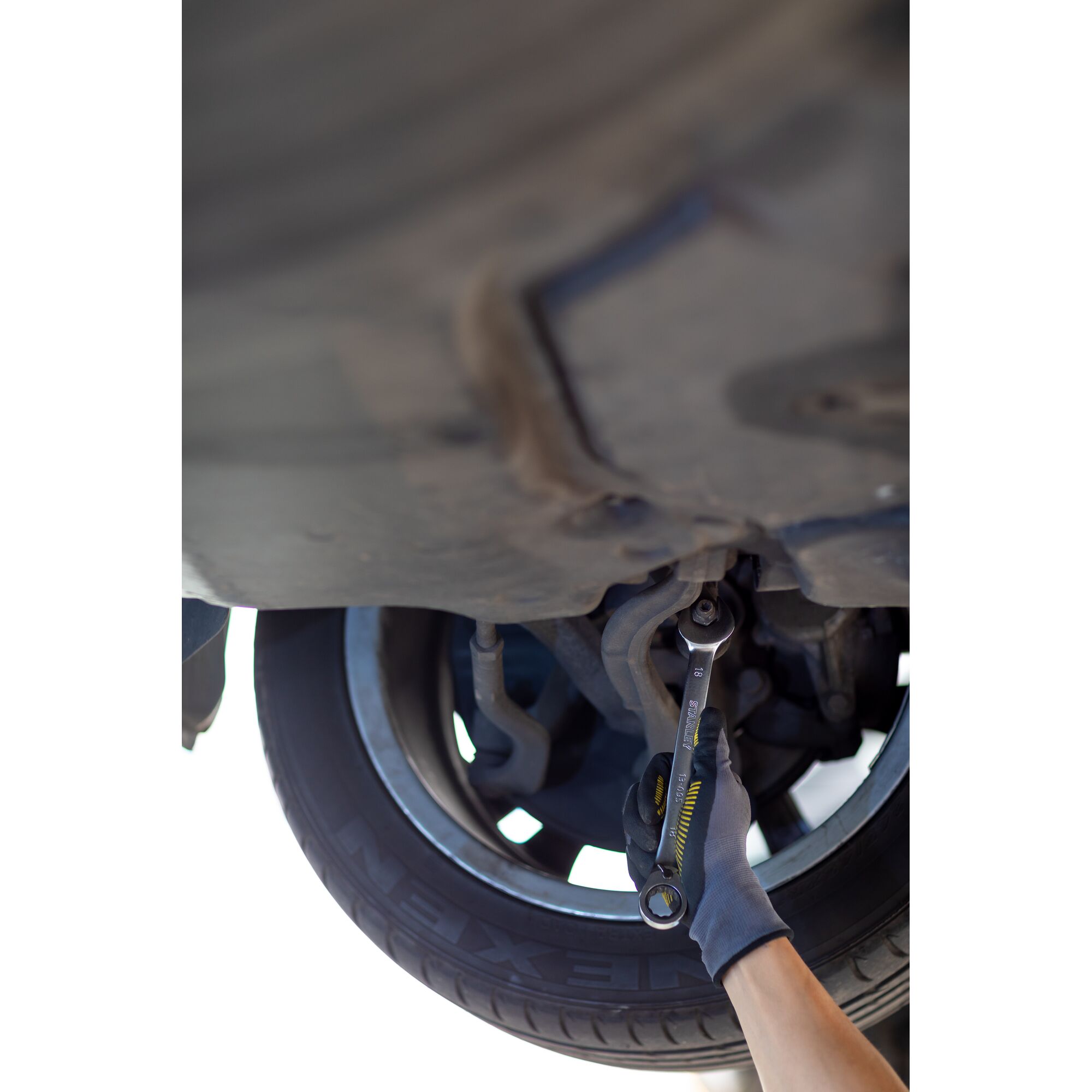 STANLEY FMMT13089-0 wrench used under car near wheel, photography of tool in automotive repair context.