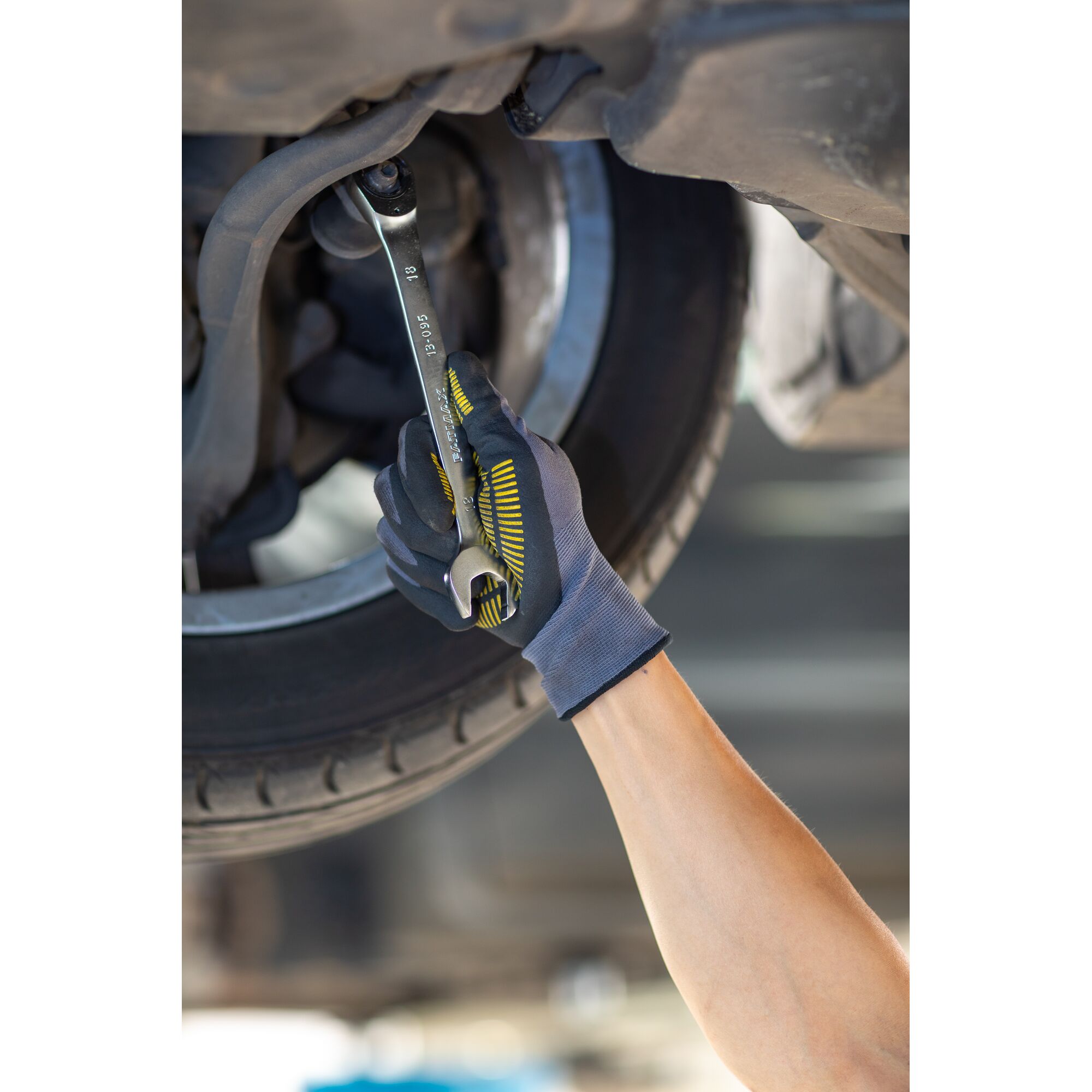 Photo of STANLEY FMMT13094-0 wrench in use by gloved hand repairing car undercarriage, automotive context.