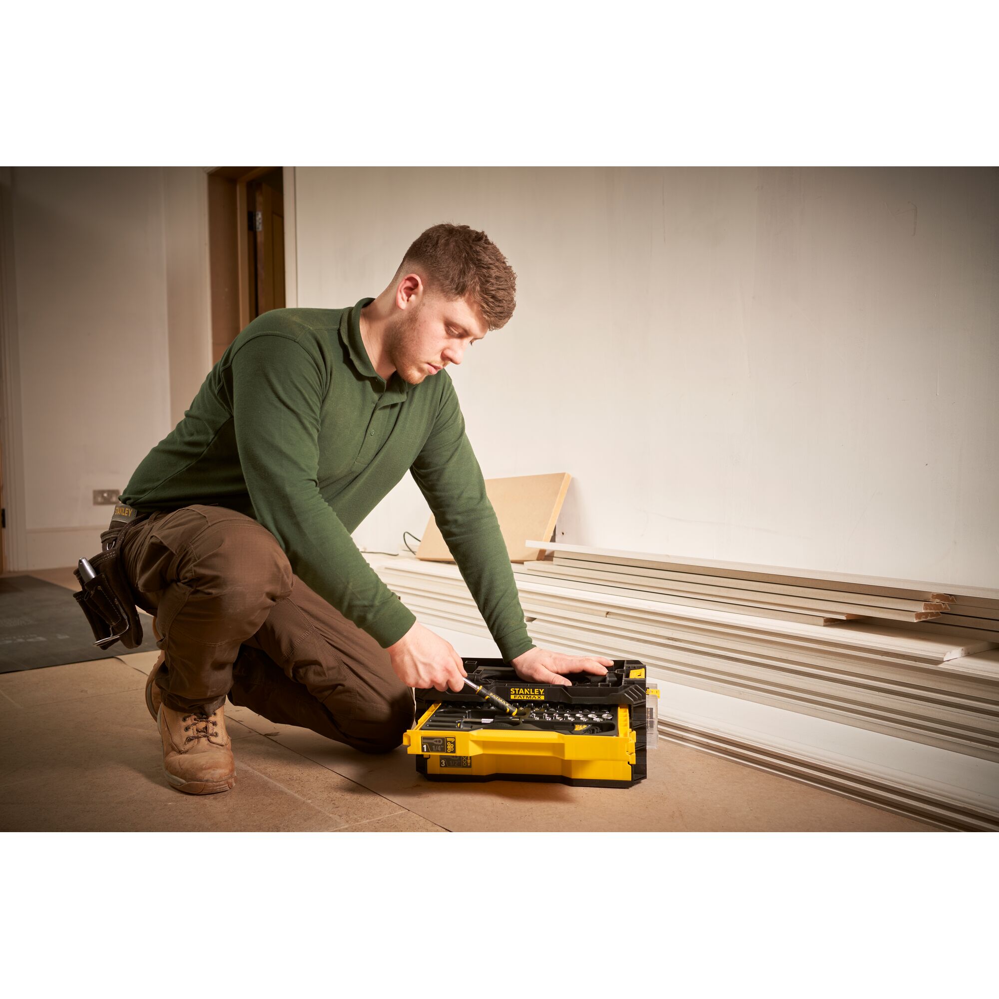 Photo of STANLEY FMMT98107-1 yellow tool box with hand tools, used by a worker kneeling indoors.