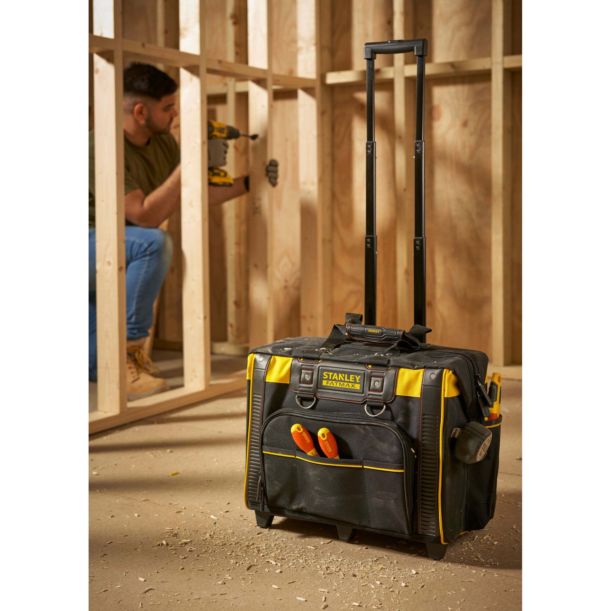 STANLEY FMST1-80148 rolling tool bag with handle, black and yellow, at construction site, front angle.