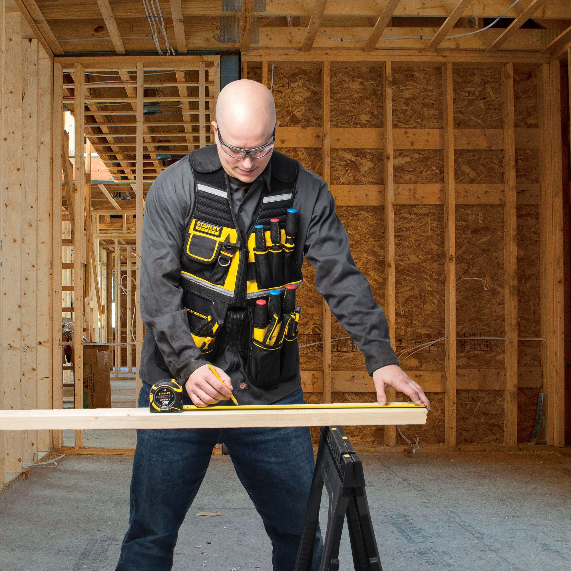 STANLEY FMST530201 tool vest with multiple pockets, worn by a person measuring wood in a construction site.