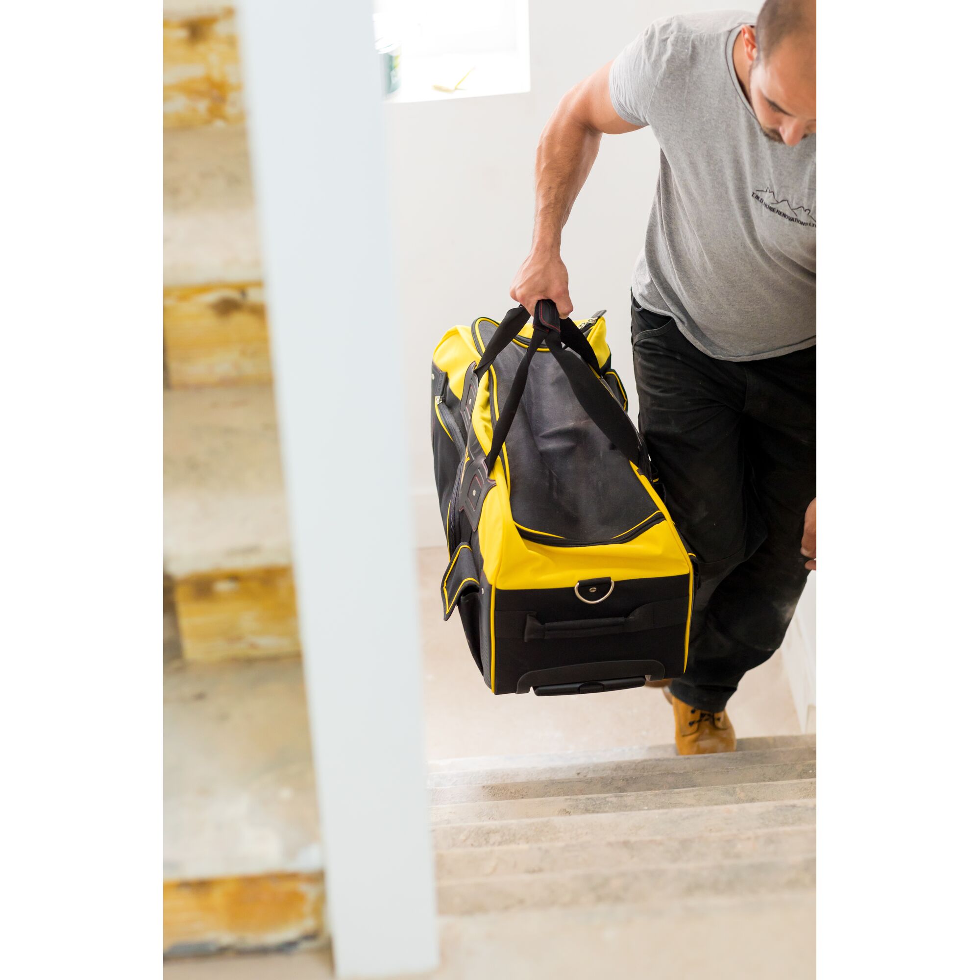 STANLEY FMST82706-1 large yellow and black tool bag carried up stairs, lifestyle context.
