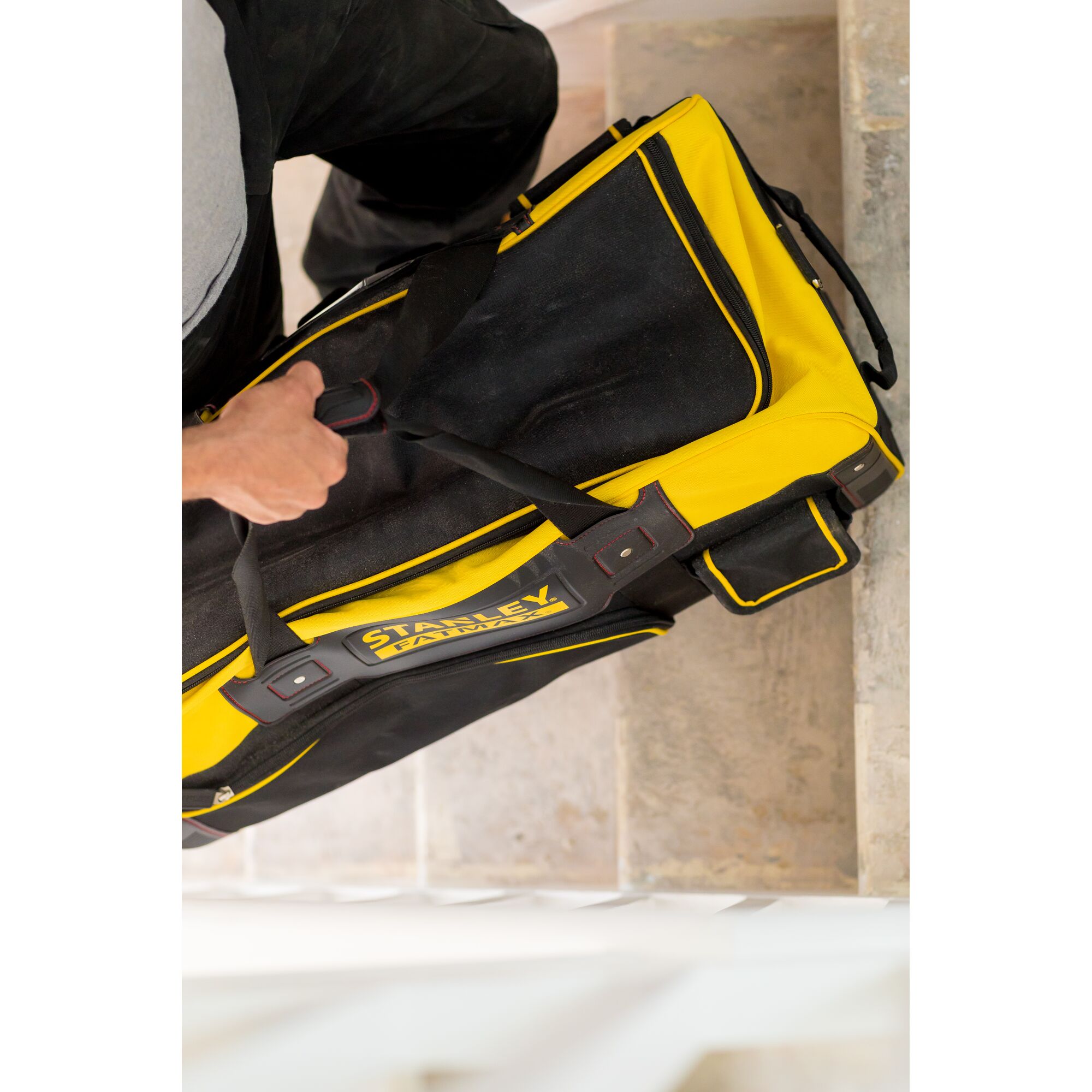Photo of a STANLEY FMST82706-1 tool bag in black and yellow carried by hand, shown from above on stairs.