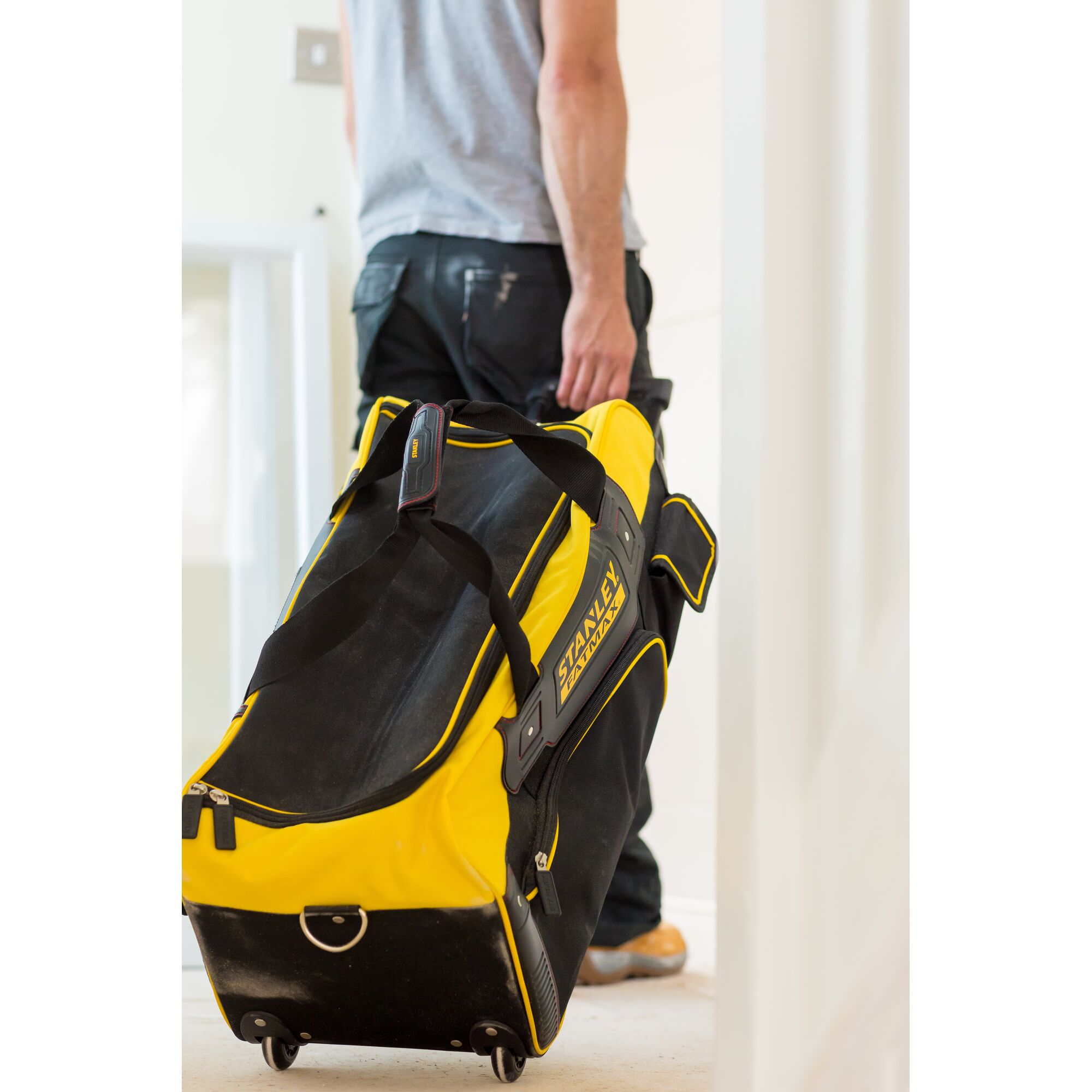 STANLEY FMST82706-1 rolling tool bag, black and yellow, photographed in use being pulled by a person.