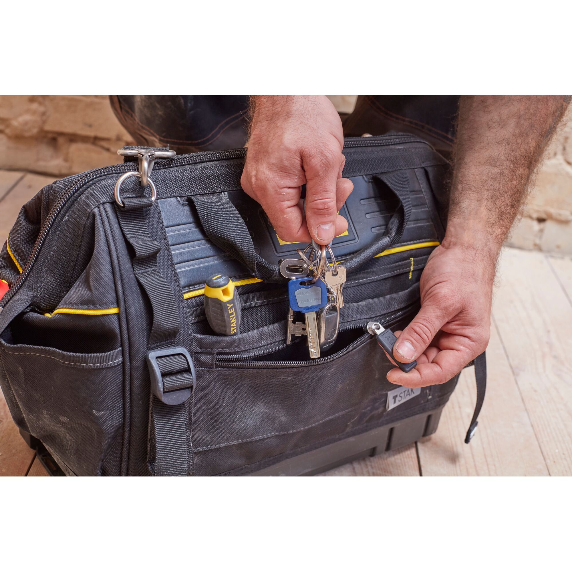 STANLEY FMST83297-1 tool bag, front angle, black with yellow accents, keys and screwdriver in pocket.