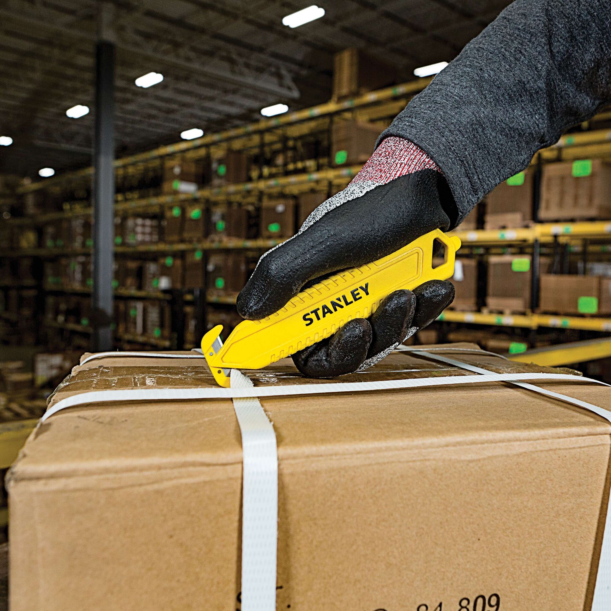 STANLEY STHT10359 yellow safety utility knife cutting box strap, close-up in warehouse.