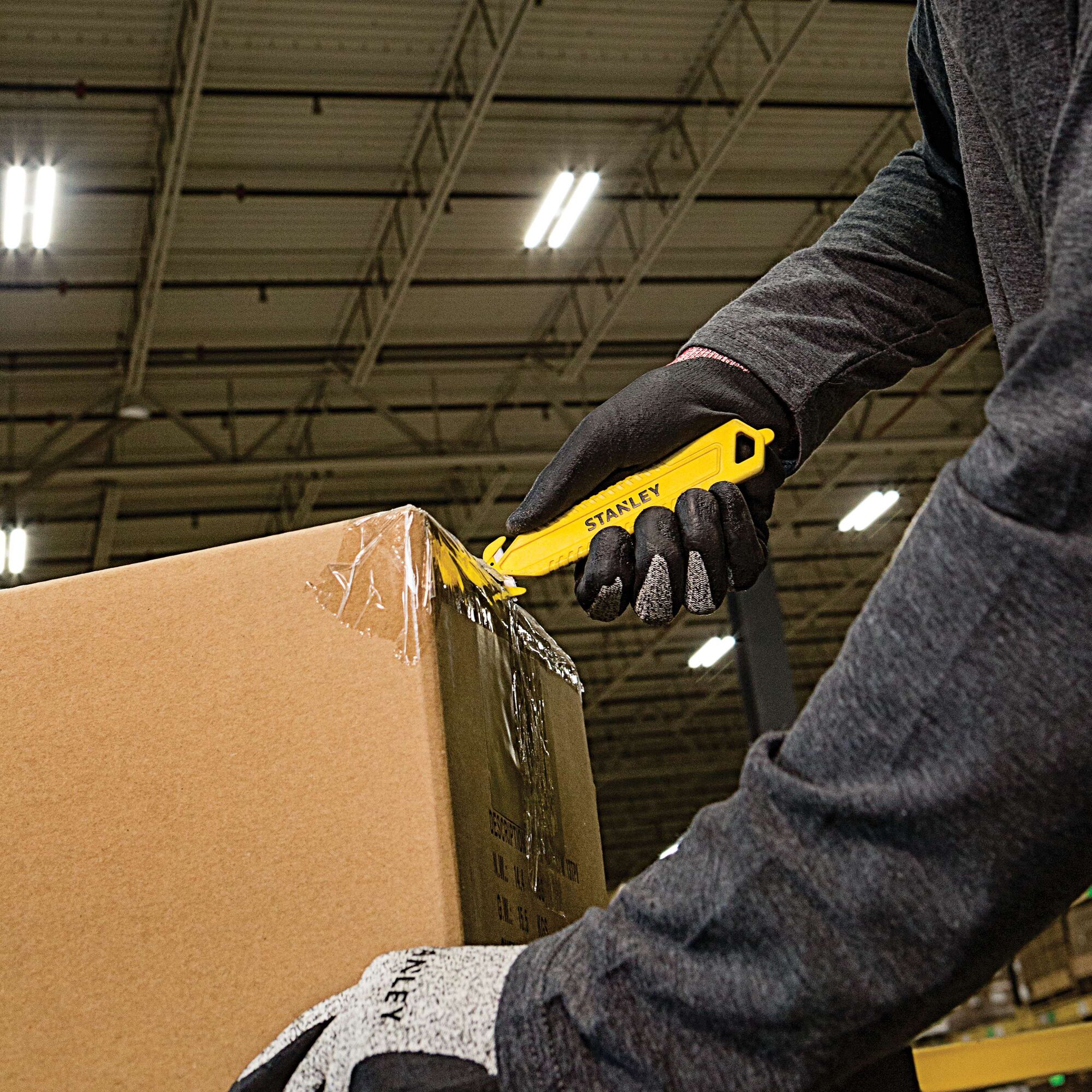 Photo of a person using a STANLEY STHT10359 utility knife to open a cardboard box in a warehouse.