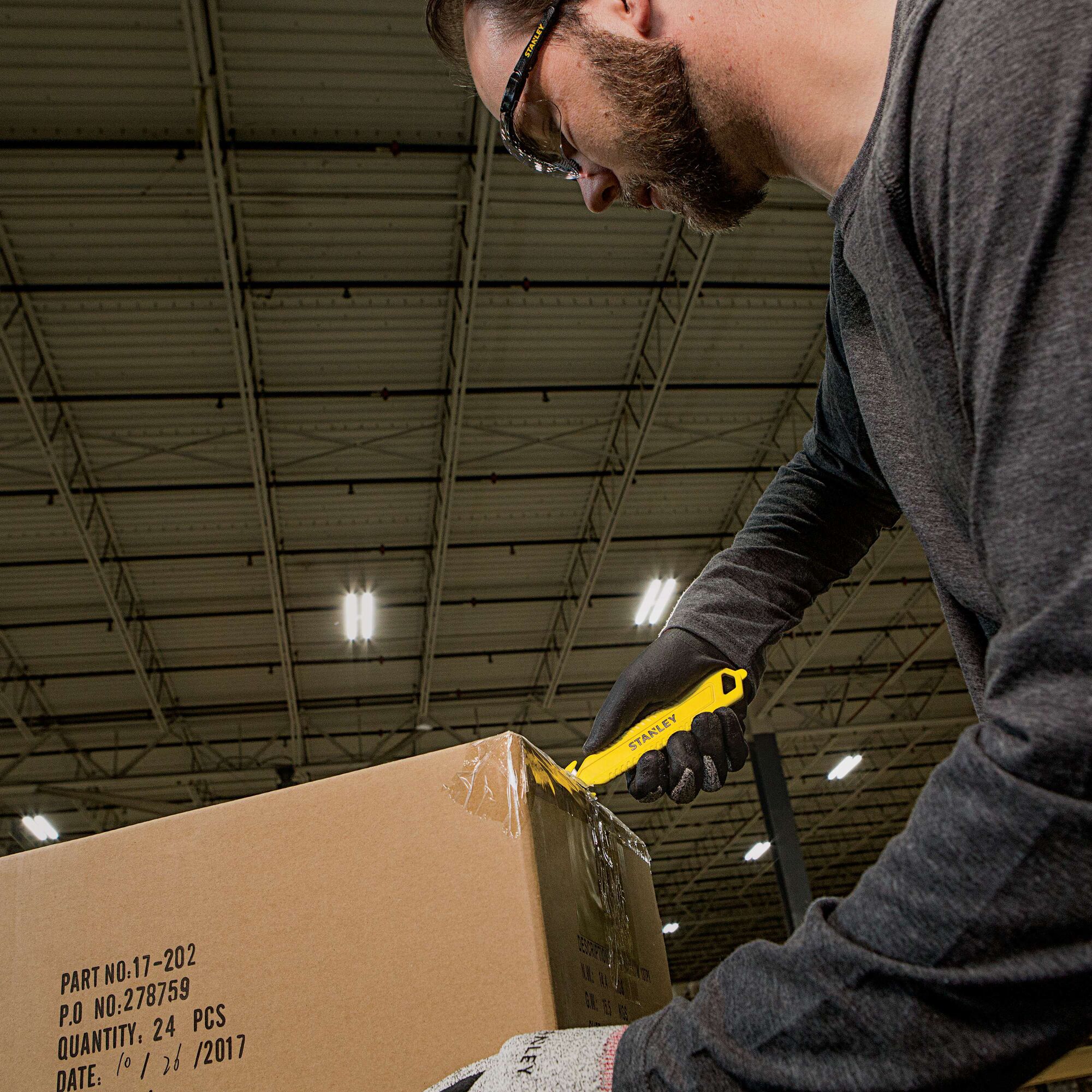 Stanley STHT10359 utility knife cutting box tape in warehouse, visible yellow tool in use.
