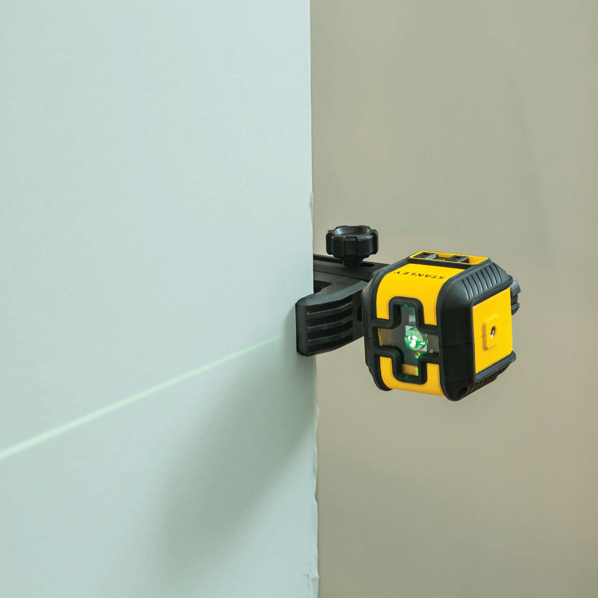 STANLEY STHT77499 laser level photography, side angle showing yellow and black device clamped to a wall emitting green laser.