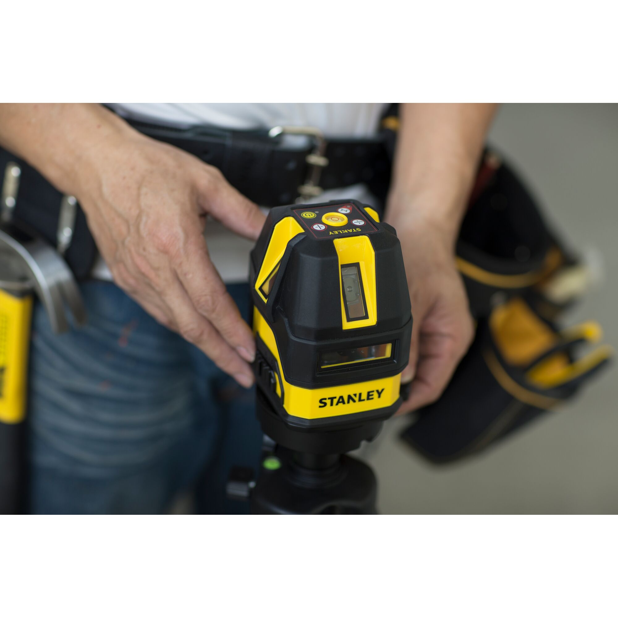 Stanley STHT77513-8 yellow and black laser level held by a person with a tool belt, front view.