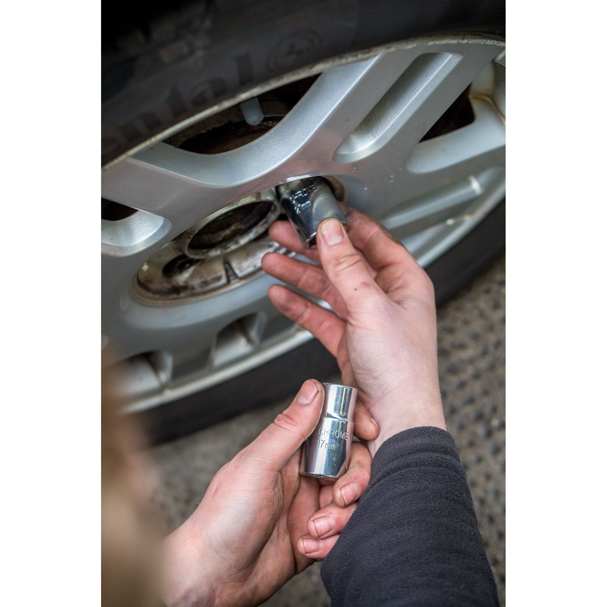 Photo of hands using STANLEY STHT80890-0 socket on car wheel lug nut, close-up, automotive tool in use.