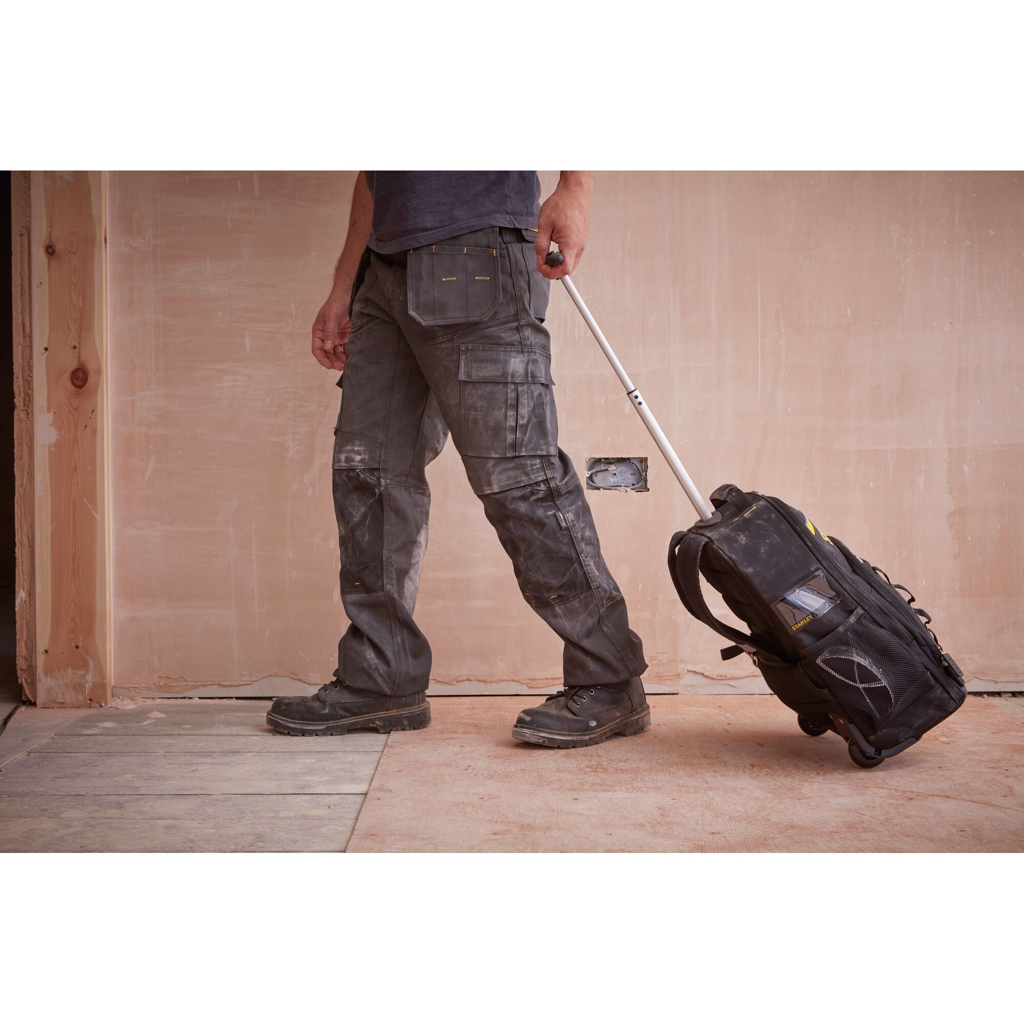 STANLEY STST83307-1 rolling tool backpack on construction site, side angle, black with yellow details.